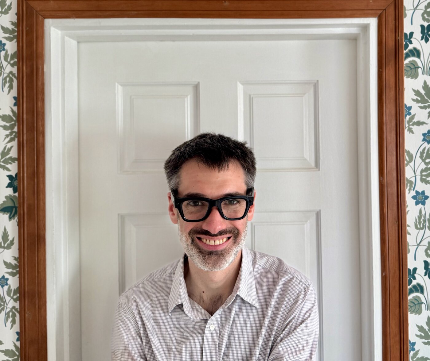 Daniel Sito — dark-framed glasses, smiling, in a panelled doorway